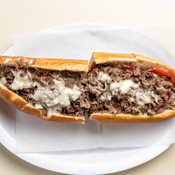 A Randazzo's Pizzeria cheesesteak, cut in half, filled with steak, melted cheese, and red peppers.