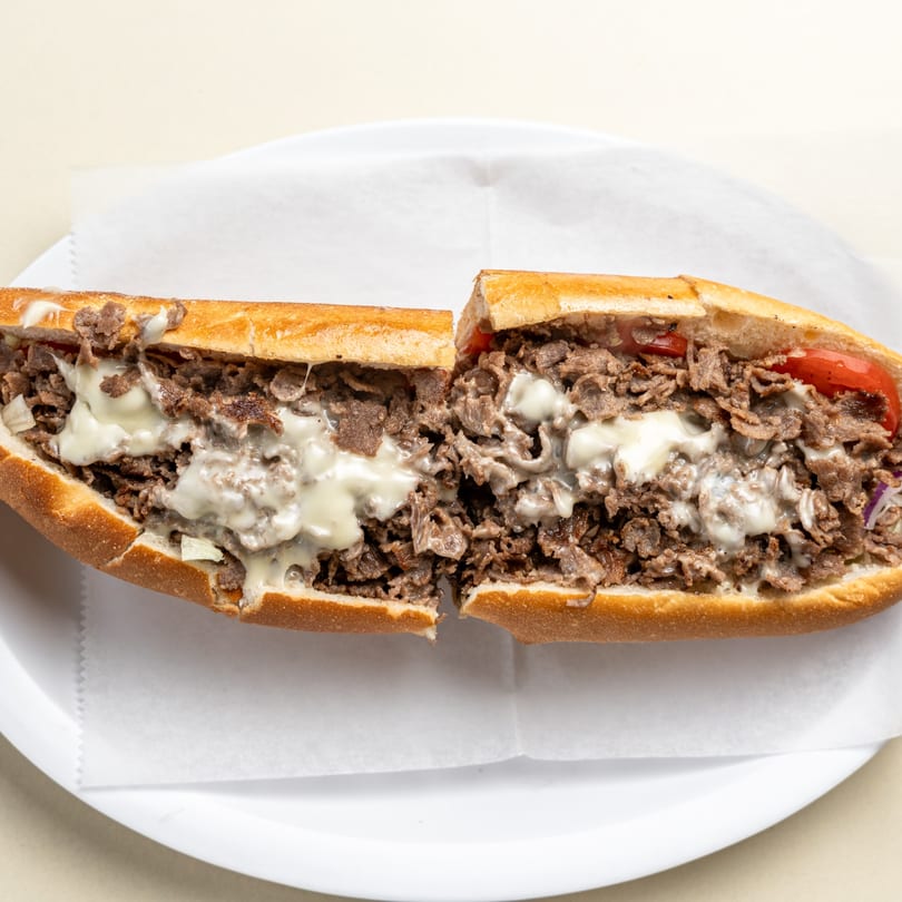 A Randazzo's Pizzeria cheesesteak, cut in half, filled with steak, melted cheese, and red peppers.