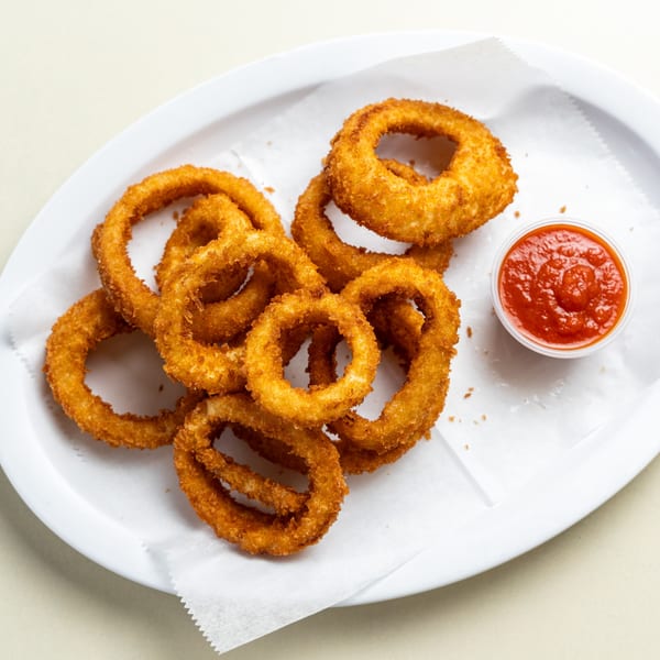 Golden-brown onion rings with a side of red dipping sauce on a white plate with parchment paper.