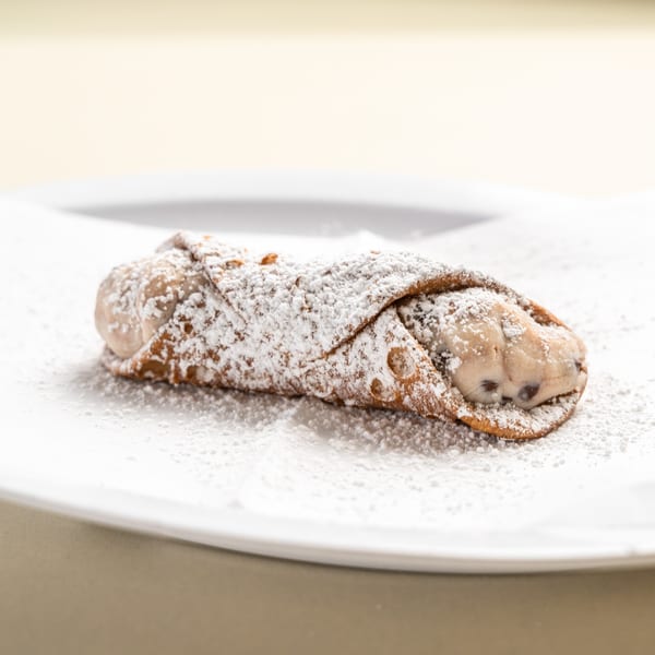 A single Randazzo's Pizzeria cannoli, dusted with powdered sugar, on a white plate.