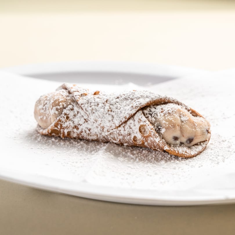 A single Randazzo's Pizzeria cannoli, dusted with powdered sugar, on a white plate.