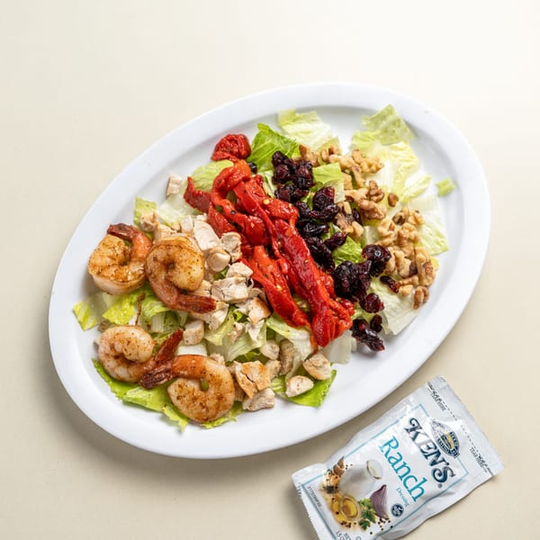 A salad with lettuce, shrimp, chicken, roasted red peppers, dried cranberries, walnuts, and ranch dressing.