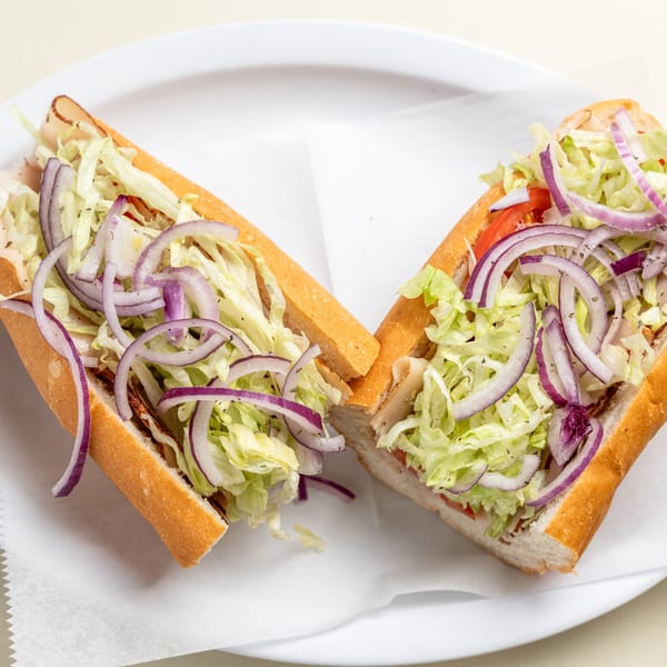 A Randazzo's Pizzeria sub sandwich, cut in half, filled with meat, lettuce, tomatoes, and red onions.