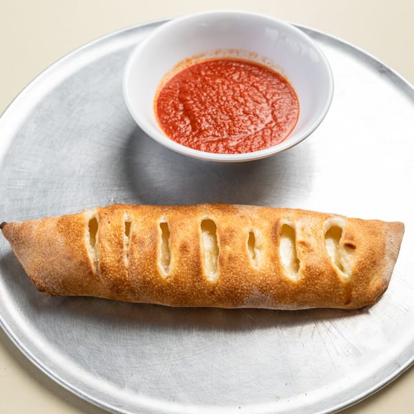 A golden-brown Randazzo's Pizzeria calzone with cheese filling, served with a side of red marinara sauce.