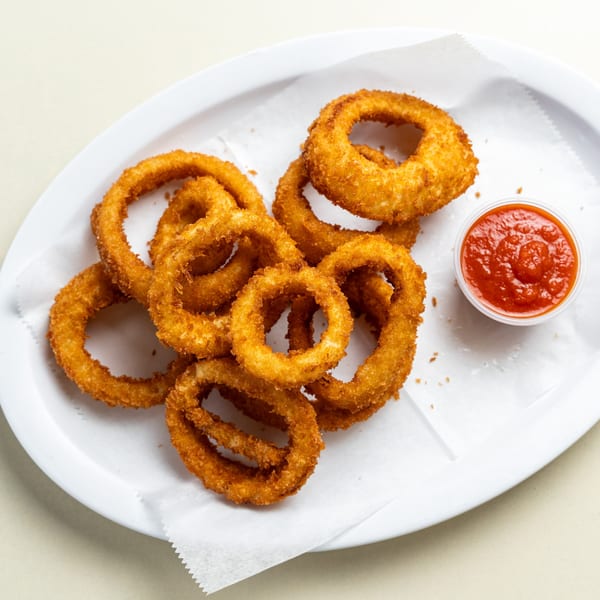 A white platter of golden-brown onion rings with a side of red marinara sauce.